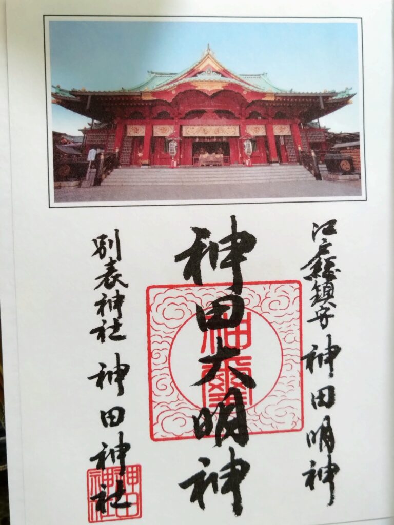 神田明神御朱印原始照片，中央社名墨書與朱印，上方附有朱紅社殿照片
